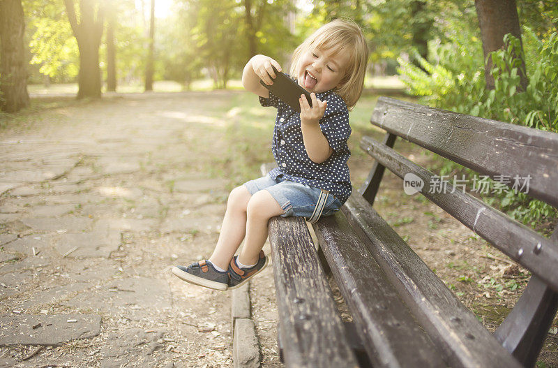 小孩坐在公园的长椅上自拍