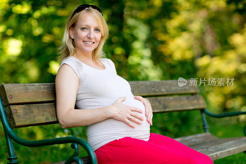 女人触摸怀孕的肚子公园长椅