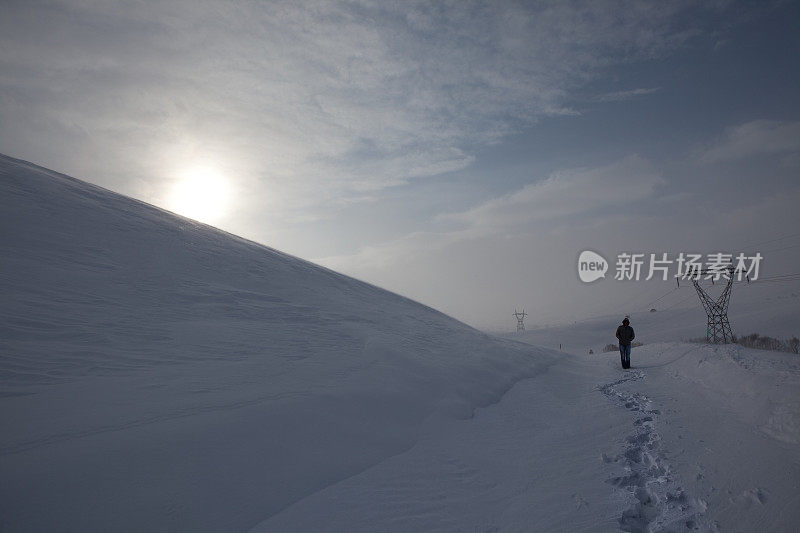 一个孤独的人走在夕阳下的雪地上