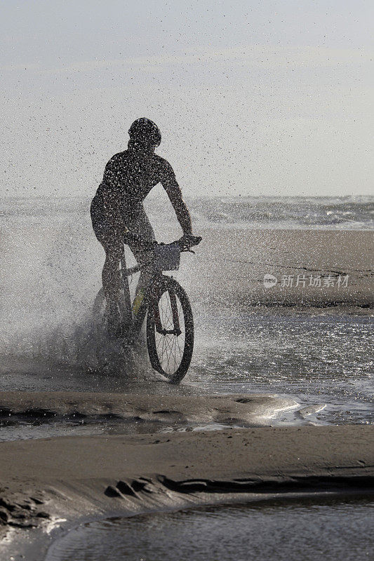 骑自行车的剪影在海水中溅起水花