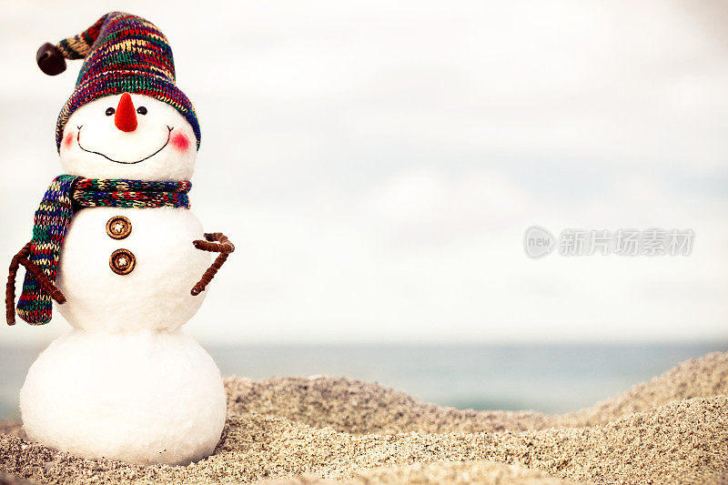 在阳光明媚的海滩上，雪人戴着红色的圣诞老人帽和太阳镜。新年贺卡的假日概念