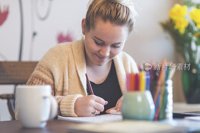 一位妇女在家用铅笔涂色一本成人涂色书