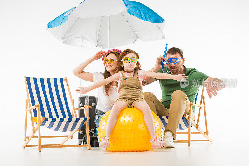 家人在游泳护目镜与遮阳伞，太阳躺椅和球孤立在白色