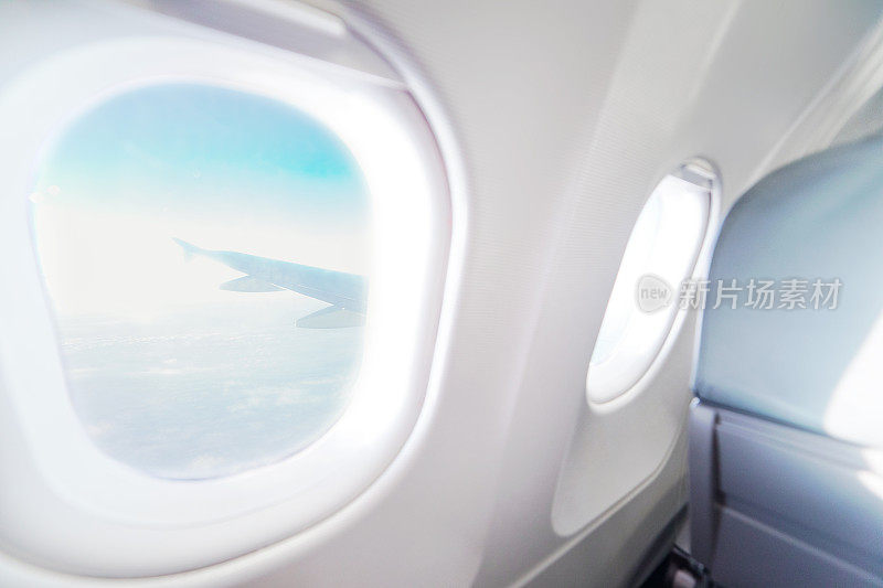 飞机内部的飞机窗口视图。飞机的窗口。度假目的地的概念。浅蓝色的座位和白色的内部与天空和机翼的视野