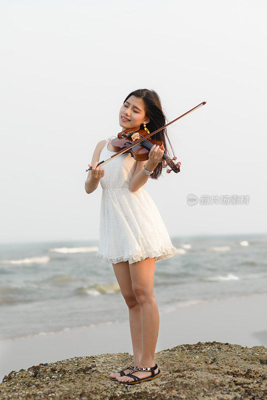 在海滩上拉小提琴的快乐女人。
