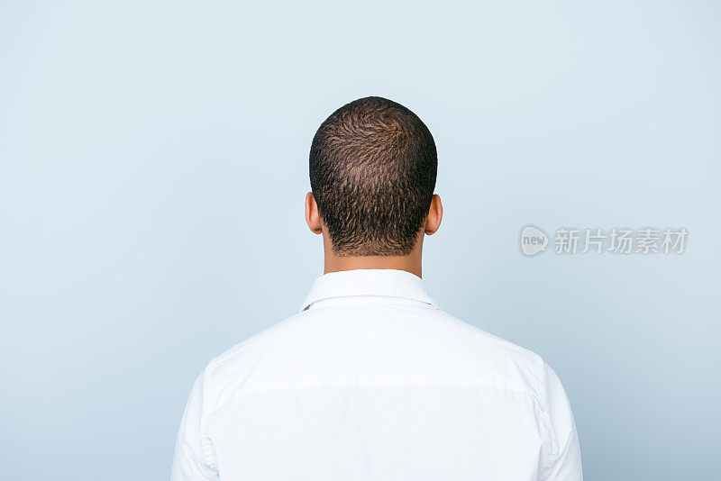 后视图的一个美国穆克拉托人，在漂亮的白色正式衬衫，站在一个纯蓝色的背景。吸附模型。头发护理的概念
