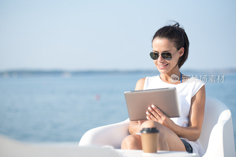 年轻女子拿着平板电脑坐在海边的酒吧里