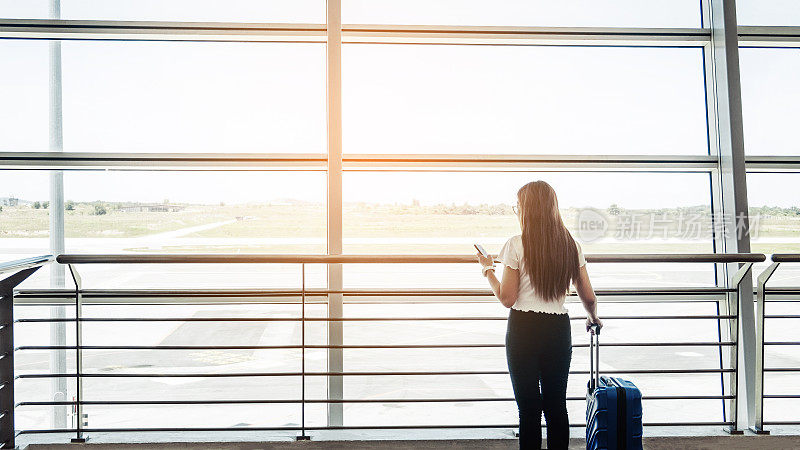 亚洲旅行者女性寻找航班在机场航站楼智能手机旅游概念