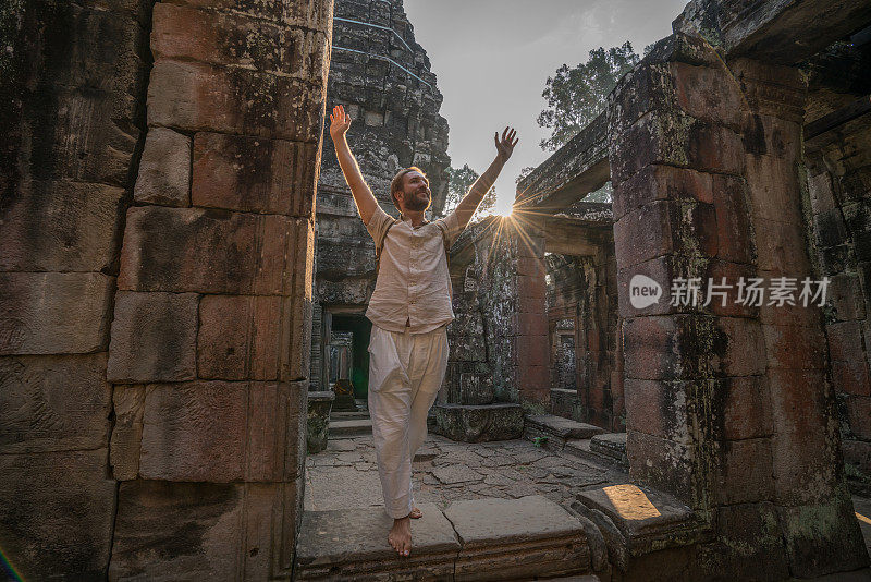 一名年轻男子在柬埔寨参观吴哥窟的庙宇，他张开双臂站着。人们旅游发现亚洲的概念。日落时分，只有一个人，在东南亚暹粒冒险和探险。