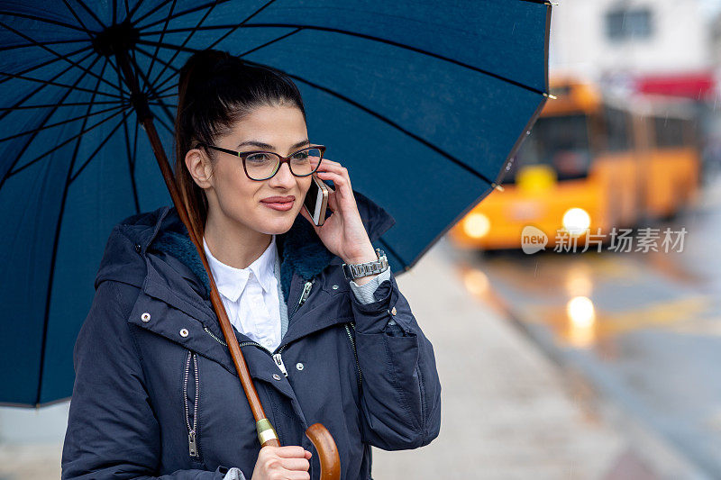 美丽的年轻女子在雨中走在街上，拿着一把伞。