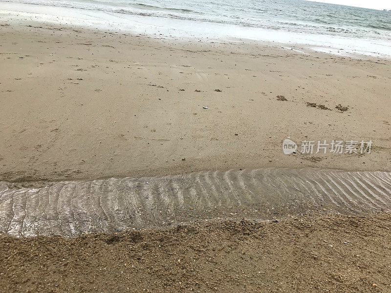 影像浅浅的水道在沙滩上留下了一天，温柔的涟漪，潮水拍打着海边的海岸线和潮湿的沙滩沿着海滨，复制空间为文字，蠕虫投在沙子