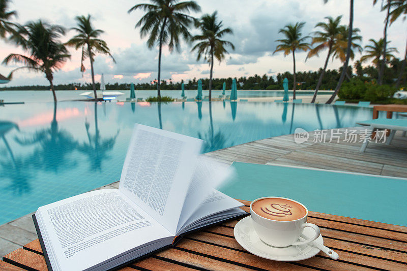 日落时分，在游泳池旁边的木桌上打开一本书和一杯咖啡