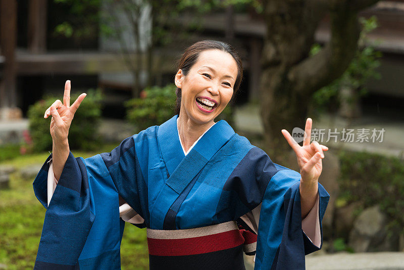 快乐成熟的日本妇女在传统和服微笑举起双手和平的手势