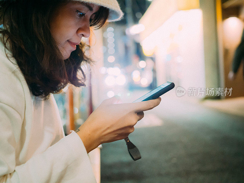 亚洲女人晚上在城市街道上用智能手机发短信。