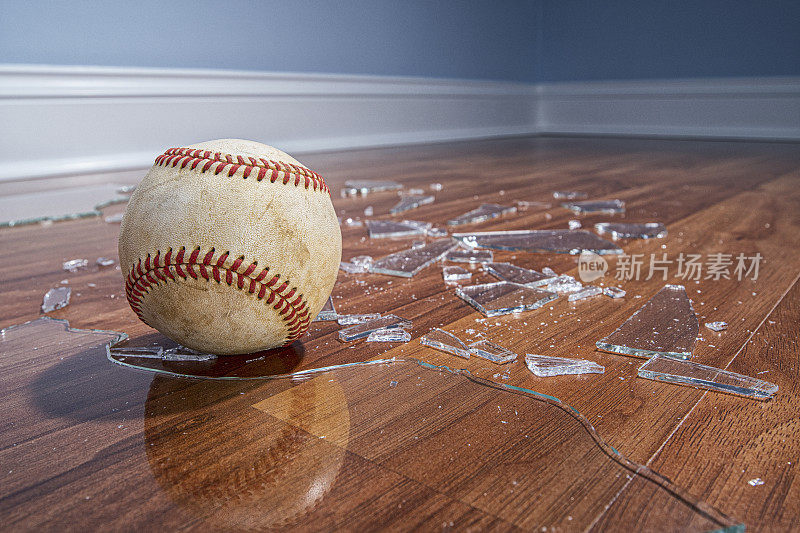 从地板上的一扇窗户看到的带有破碎玻璃的棒球的低角度视图