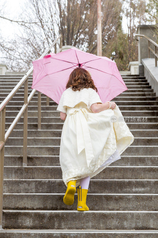 带着明亮的雨伞和靴子爬室外楼梯的可爱女孩