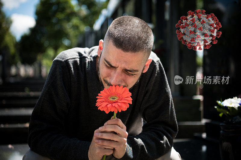 悲伤和沮丧的鳏夫在黑衣跪在墓碑前，拿着一朵花和哀悼家人的损失。死亡、哀悼、葬礼和精神的概念——Covid-19