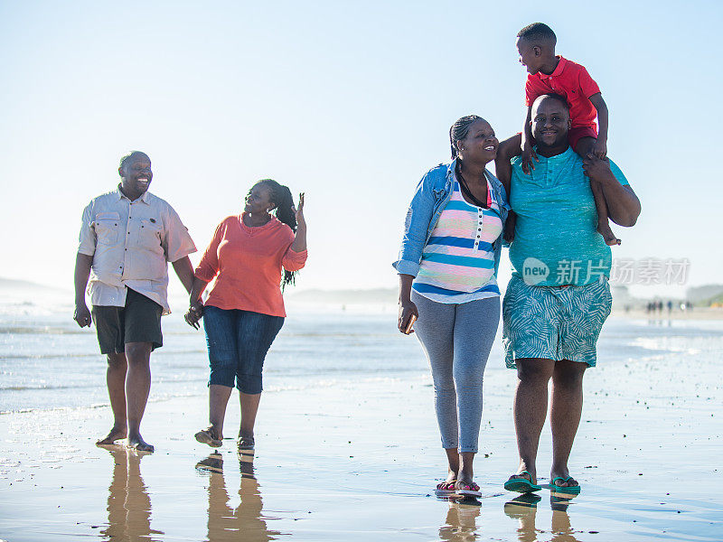 几代同堂的一家人一起赤脚在海滩上散步