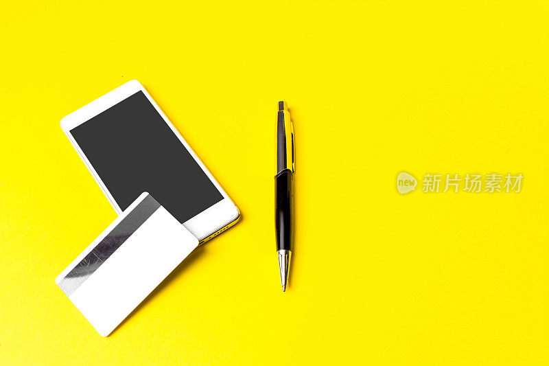 黄色背景的智能手机，名片和钢笔。在线购物。在线支付。