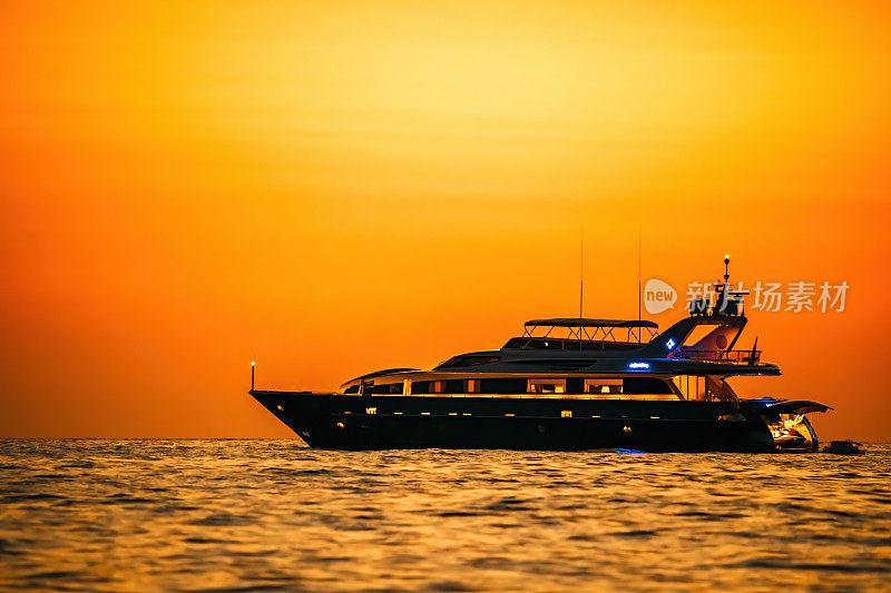 金色浪漫的日落在私人现代豪华游艇停泊在海上-豪华假日和旅游概念。海面上燃烧着的红色夕阳和时髦游艇的剪影