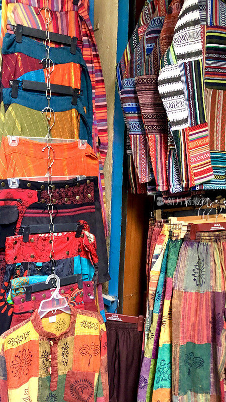 户外市场摊位展示的民族嬉皮风格的服装挂衣架，裤子，裙子和上衣