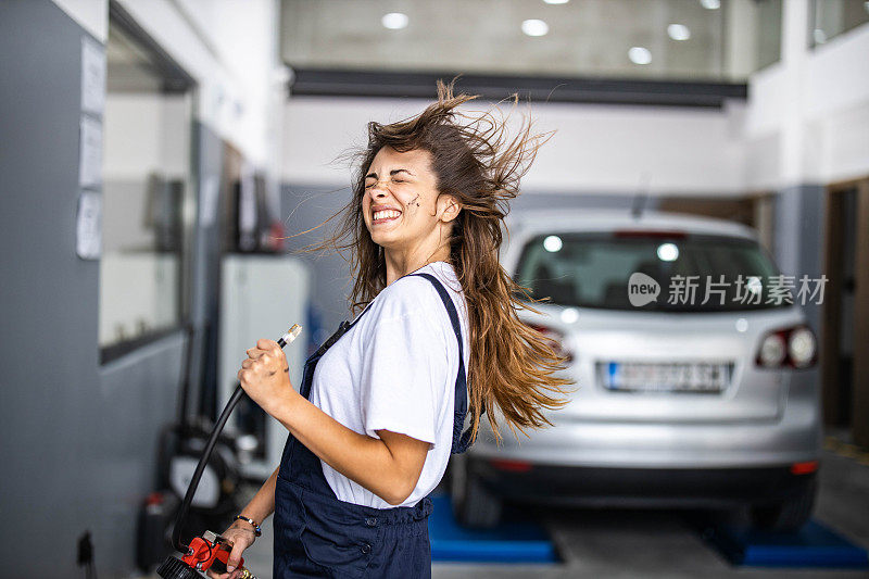 好玩的女性汽车技工吹空气到她的头从一个泵在车间。