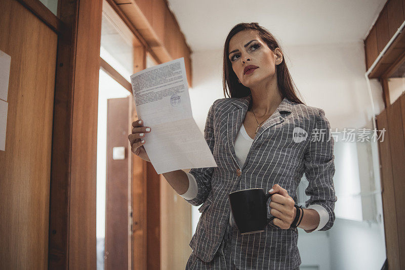 一位女商人端着一杯咖啡，手里拿着一份文件等待检查