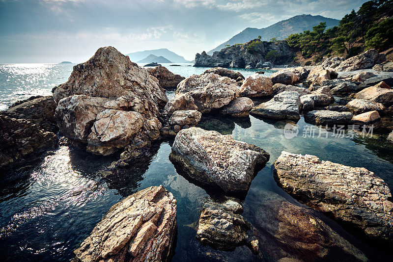 地中海岩石海岸。大的石头。阳光反射在水中。背景光