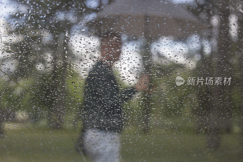 一个成年人带着雨伞在雨天出门散步