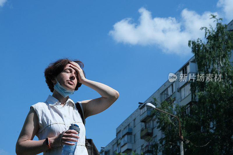 一个成熟的女人在炎热的夏天在城市的街道上喝水