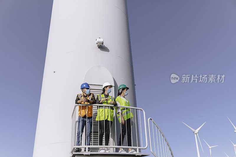 戴着防护口罩的男女工程师在大流行期间在风电场的风力涡轮机上工作