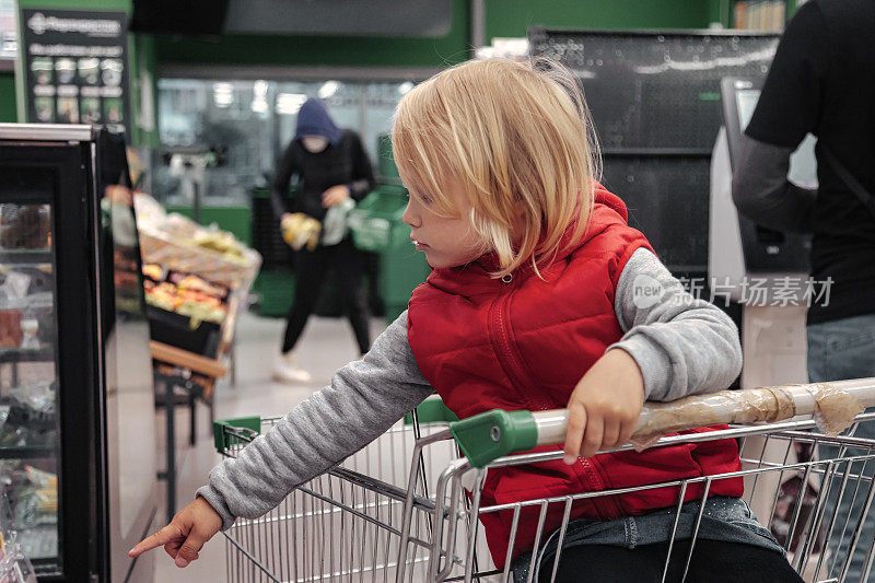 小女孩坐在商场或超市的购物车里买东西