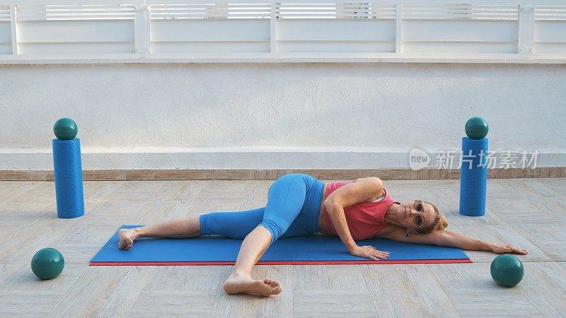 健身妇女侧躺在运动垫上，腿在身体前面