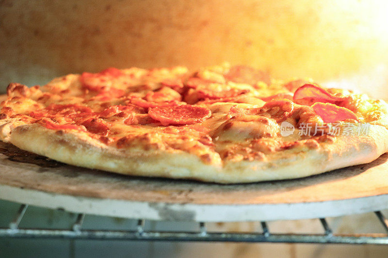 自制辣香肠披萨在烤箱中烘烤的全帧图像，在披萨石头上烤脆的基底，磨碎的马苏里拉奶酪和辣香肠切片，重点放在前景