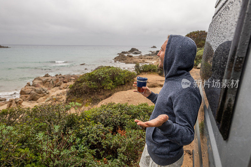 男人在他的露营车外喝茶，看海景