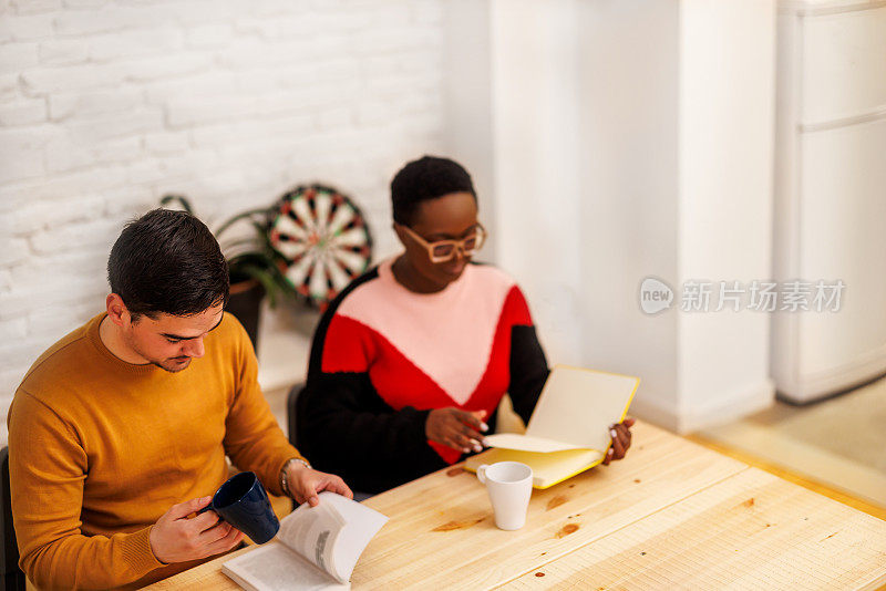 这是一张白人男子和非裔美国妇女的照片，他们正在用餐厅里看书，坐着等着吃饭。真实的生活概念。