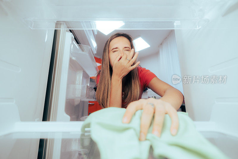 不开心的女人用布清洁又臭又脏的冰箱