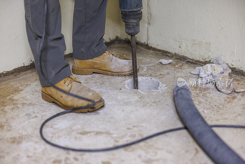 图为，一名工人正在用钻头在地下室地板上打洞，以便安装氡缓解系统。