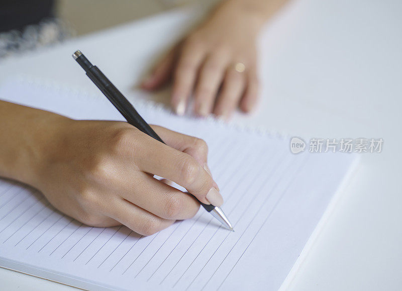 特写一个女人的手与钢笔写在笔记本上