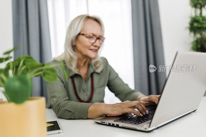 老年妇女使用笔记本电脑和工作在家里