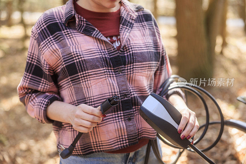 充电后，女子的手从插座上拔下电动汽车适配器。