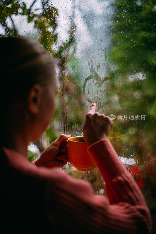 一个女人在雨天喝咖啡，在窗户上画心