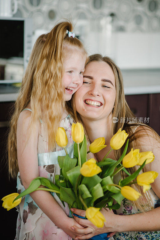 女儿在家里的厨房里向妈妈祝贺，并送上一束黄色的郁金香花。母亲节的概念。妈妈和小女孩拥抱微笑。妇女节贺卡。特写镜头