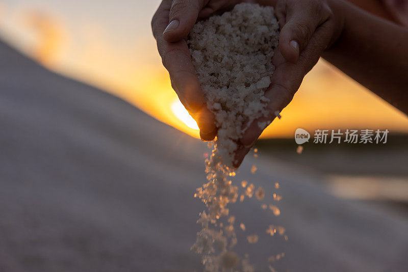 裁剪图像的妇女倒盐在地上在日落。