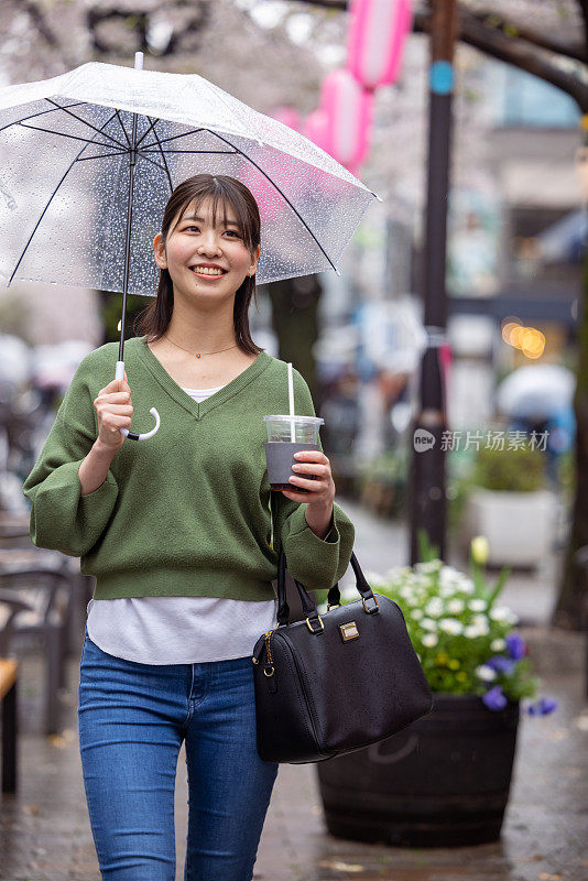 年轻女子走在樱花下在城市在一个雨天-露齿微笑