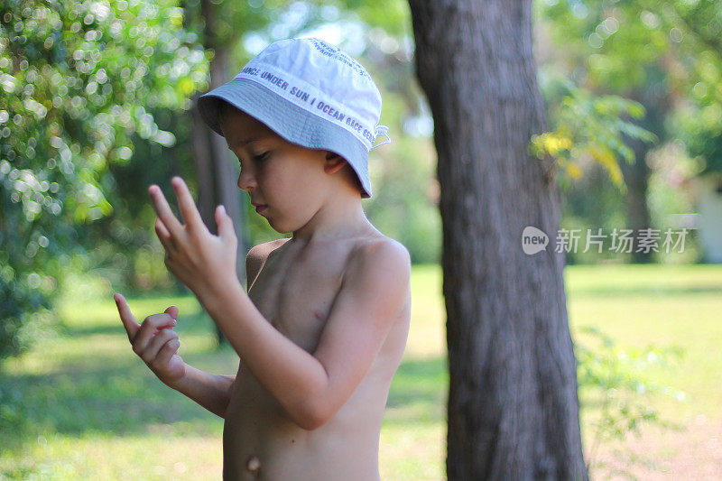 夏日公园里，一个没穿t恤、头戴帽子的男孩在手指头上热情洋溢地想着什么。经济度假的概念。