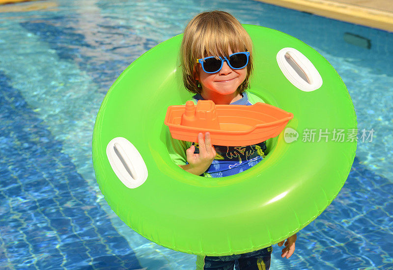 积极的男孩，有一个充气圈和一个床垫在游泳池附近。在度假胜地度假的孩子。家庭旅馆