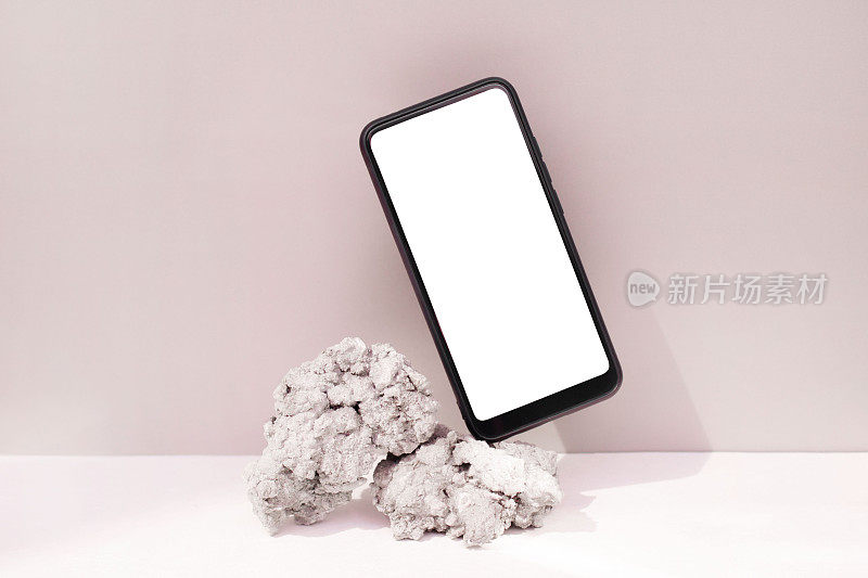 模型模板智能手机平衡在粉红色背景上的天然石材。手机与空白屏幕模板