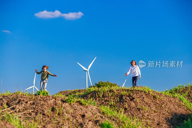 孩子们在农村的绿色山丘上玩耍，旁边是风力涡轮机