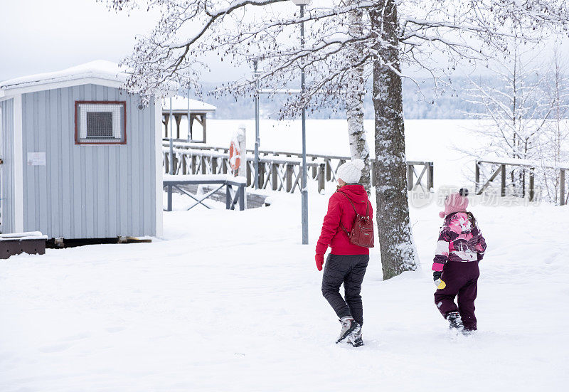 一个年轻的女人和一个8岁的小女孩，在湖边一个下雪的公园里。